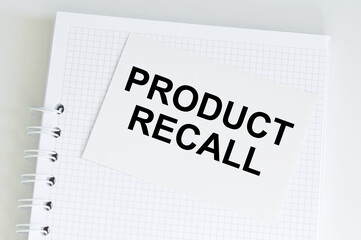Product Recall text on a white card against the background of a blank notepad page on a desk, a...