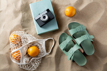 leisure and summer holidays concept - slippers, string bag of oranges, film camera and book on...
