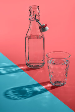 Vintage bottles and glass with sun light shadows or reflection on pink-blue background.