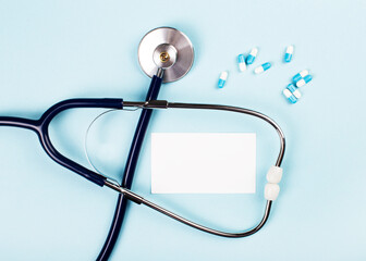 On a blue background, a stethoscope, pills and a white card with a place to insert text. View from above. Mockup. Medical concept