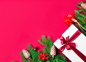 Beautiful Christmas gift box on a red background next to fir branches and Christmas decor. Festive new year concept