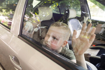 Child locked in car. Blond boy is closed in auto without water. He is hot and his face is red. Irresponsible parents left the child alone in a hot car. Concept of poor care for kids.