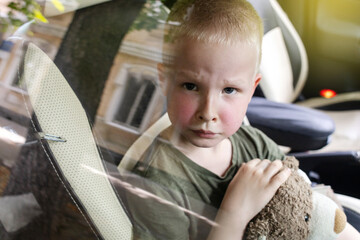Child locked in car. Blond boy is closed in auto without water. He is hot and his face is red. Irresponsible parents left the child alone in a hot car. Concept of poor care for kids.