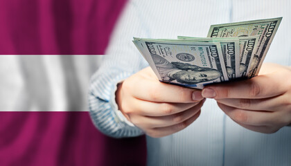 Human hands holds American dollars money on Latvian flag background. Currency exchange, banking and business in Latvia concept.