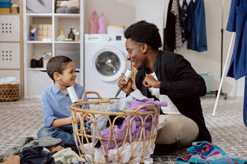 Dad fooling around with son while cleaning, doing household chores. Man singing to cleaning roll of clothes removed from washing machine dried to sorted.