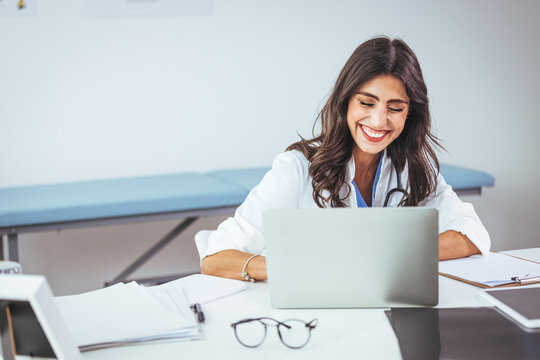 Confident female doctor sitting at office desk and smiling at camera, health care and prevention concept. Medical Doctor Indoors Portraits. Portrait of a confident doctor working at a hospital.