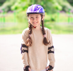 Portrait of a happy girl in a protective helmet, protective elbow pads on the background of the park. Rollerblading safely. Sport, leisure and protection concept.