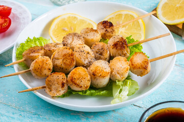 Grilled sea scallops on skewers lie on lettuce leaves. Fresh healthy snack. white plate