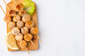 Three skewers with a grilled scallop on a wooden board, top view, free space.