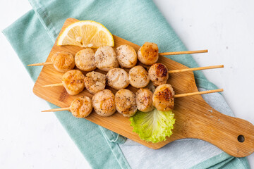 Grilled scallop fillet skewers served on a wooden board top view.