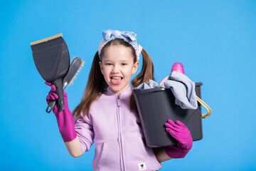 Cheerful funny little girl is holding a mop bucket, sweeper with dustpan, applied has rubber pink...