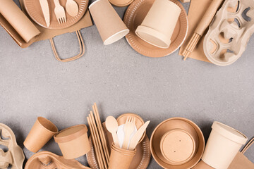 Frame made with eco paper tableware and utensils - paper cups, containers and wooden bamboo cutlery over gray concrete background with copy space. Sustainable food packaging concept