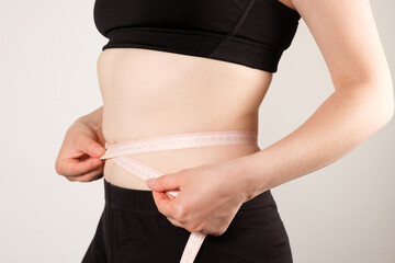 A woman measures the circumference of the abdomen with a centimeter tape, close-up. Slimming concept