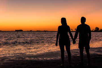 Fototapeta na wymiar Young couple in love holding hands watching one of the best sunsets ever seen by the lake. Junin, Buenos Aires, Argentina