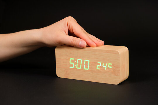 A digital clock showing a time of five o'clock in the morning and a woman's hand on a black background