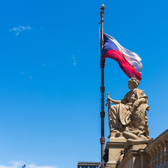 Close-up of the tricolor national flag of the Czech Republic on a bronze flagpole with a lion's head in a golden crown against a clear sky on a sunny day in Prague in front of the National Museum