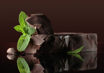 Large piece of dark bitter chocolate with mint on a black reflective background.