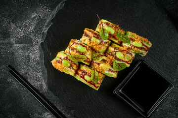 Vegetarian sushi rolls with avocado, mango and sauces isolated on a black plate. Close-up