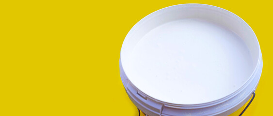 White paint in plastic bucket on yellow background.