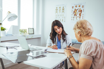 Fototapeta premium Doctor Wearing White Coat Meeting With senior Female Patient. Concerned beautiful female medicine doctor listening carefully patient complaints. Medical care or insurance concept.