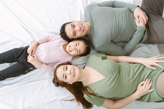 Top view of portrait of happy Asian looking at camera and smiling while lying on the floor at home. Korean or Japanese Family enjoying free and Relax time with happy moment. Weekend lifestyle concept.
