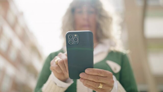 Middle age woman smiling confident using smartphone at street