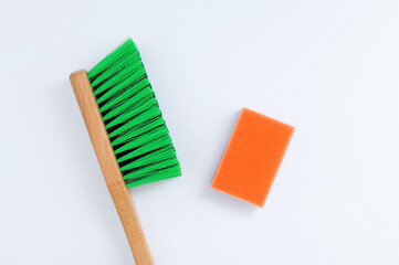 A green cleaning brush with  wooden handle and an orange cleaning sponge. White background.