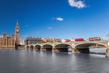 Famous Big Ben with red buses on bridge over Thames river in London, England, UK