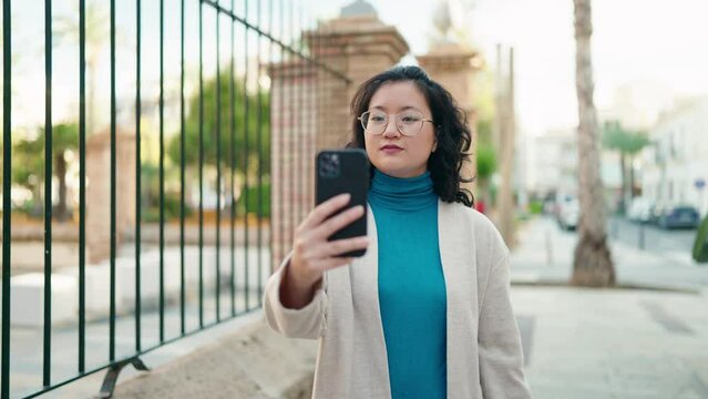 Young chinese woman smiling confident making selfie by the smartphone at street