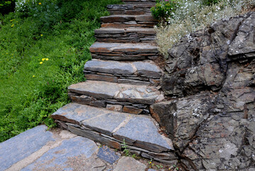 stone staircase illuminated by the morning sun. the stone is brown and joined with cement mortar. the stairs are in the rock garden or in the park - obrazy, fototapety, plakaty