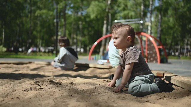 the kid is playing in the sandbox with sand. the child is having fun . Happy boy playing on the playground in the summer park