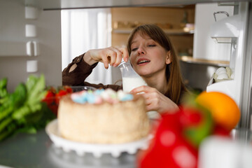 Young woman taking bottle of milk from refrigerator in kitchen