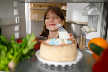 Woman enjoying fresh milk standing by the fridge