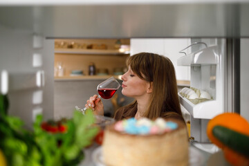 View from the inside of the refrigerator woman enjoying the taste of red wine - obrazy, fototapety, plakaty