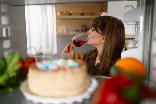 Young Woman Drinking Red Wine Standing By The Open Fridge At The Kitchen