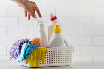 A woman's hand reaches for cleaning products for the home against a white tile background.