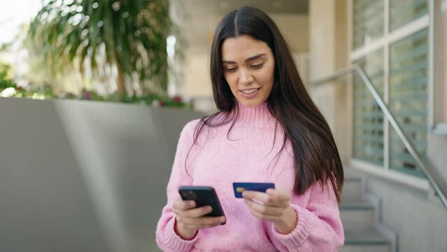 Young hispanic woman using smartphone and credit card at street