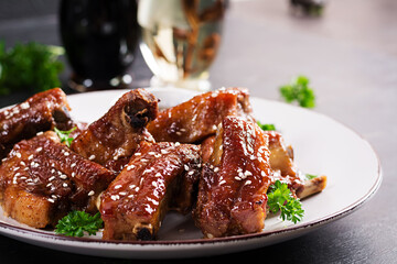 Delicious barbecued spare ribs on plate on dark background. Tasty bbq meat.