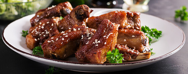 Delicious barbecued spare ribs on plate on dark background. Tasty bbq meat. Banner