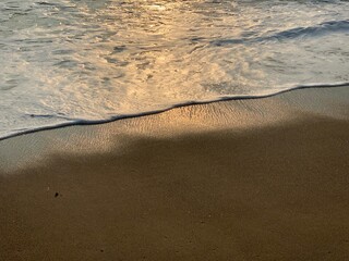 Sea foam with golden sunlight textures on the dark brown sand beach