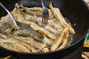 Roasting capelin in a pan on fire. Capelin fried in oil with crispy breading. Small crispy fish are fried in oil. Shallow depth of field