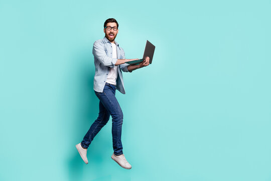 Full body photo of crazy excited person hold netbook jumping isolated on teal color background