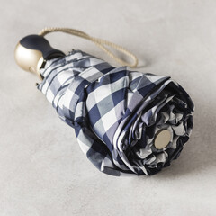 A Folded Compact Umbrella in White-Blue Squares Gray Background Square