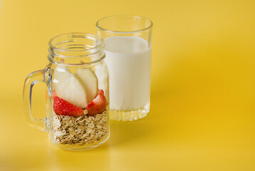 Healthy Breakfast Ingredients Homemade Granola in Glass Jar With Strawberry and Apple Glass of Milk Yellow Background Copy Space