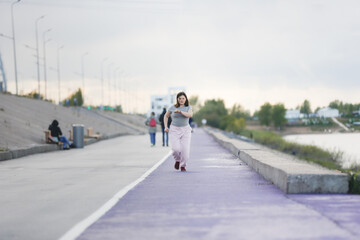 Overweight European teenage girl in tracksuit warms up, runs on violet floor concrete embankment, Sports and teenagers, overweight teenagers. Jogging helps the body to be strong.