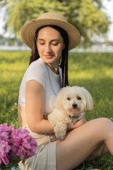 young girl with a dog. white maltese at a picnic on vacation. green bedding with food and flowers. sunny bright day.