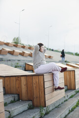 cute overweight teenager girl in tracksuit meditates, rests on wooden seat on concrete embankment