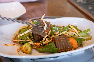 Korean traditional side dish, acorn jelly, held in chopsticks, taken at a restaurant