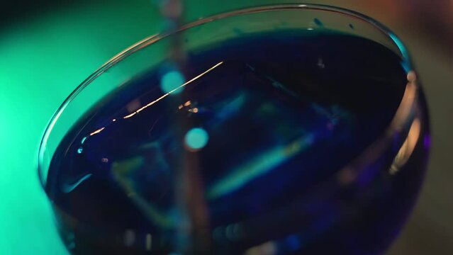 The bartender stirs a blue cocktail with ice using a bar spoon. Close-up