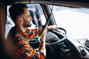 Man trucker driving in a cabin of his truck and talking on radio transmitter